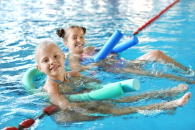 Photo of Little girls with swimming noodles in indoor pool