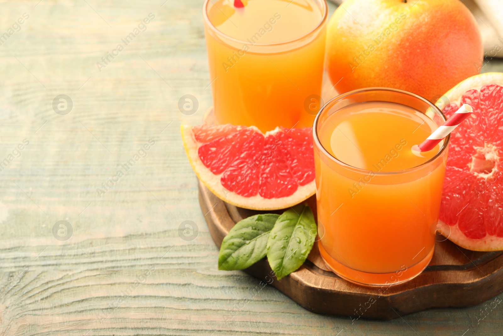 Photo of Glasses of delicious grapefruit juice on wooden table, space for text