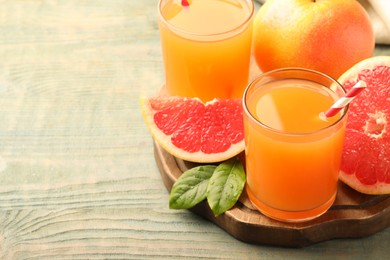 Photo of Glasses of delicious grapefruit juice on wooden table, space for text