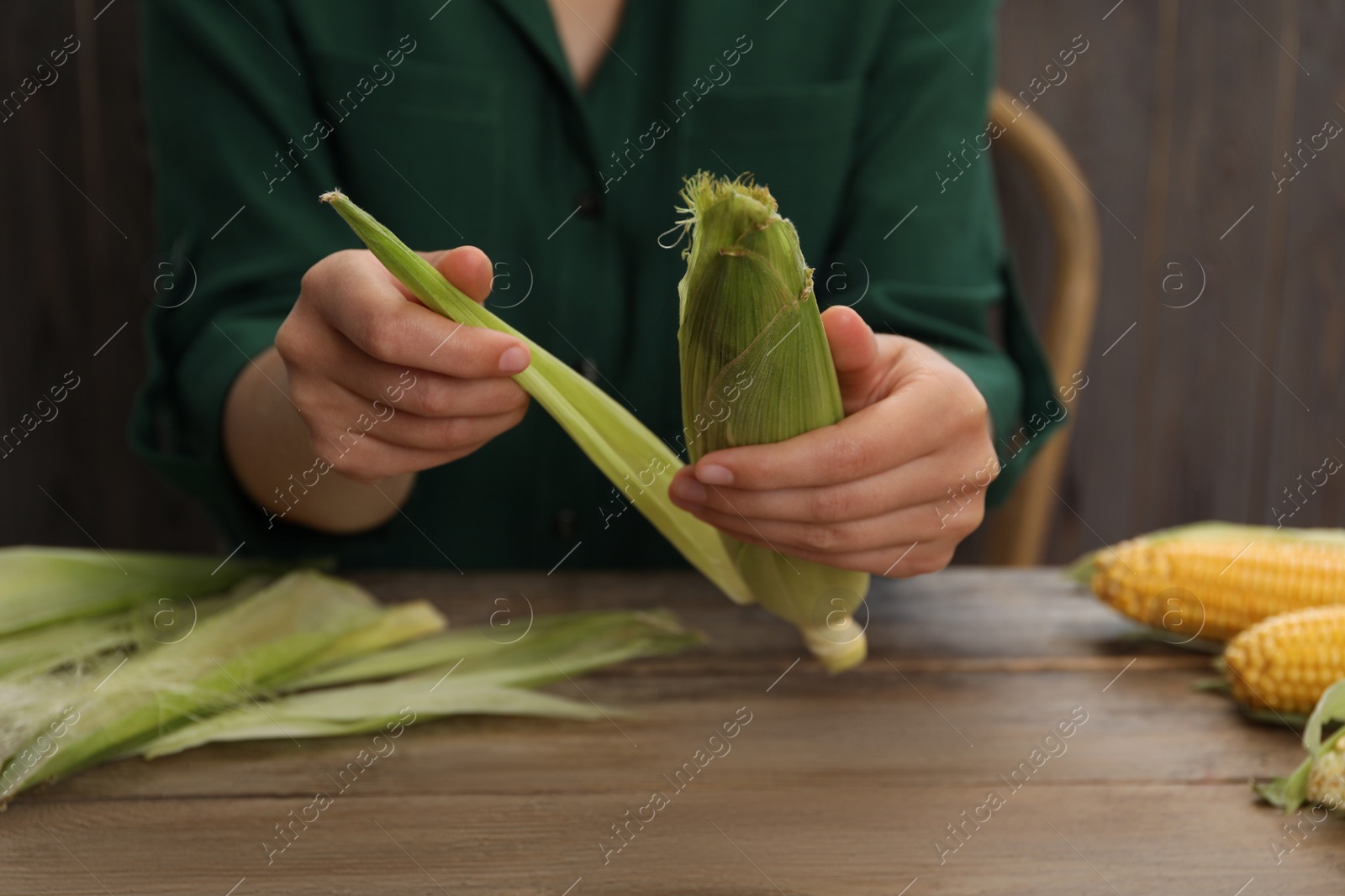 Photo of Woman husking corn cob at wooden table, closeup