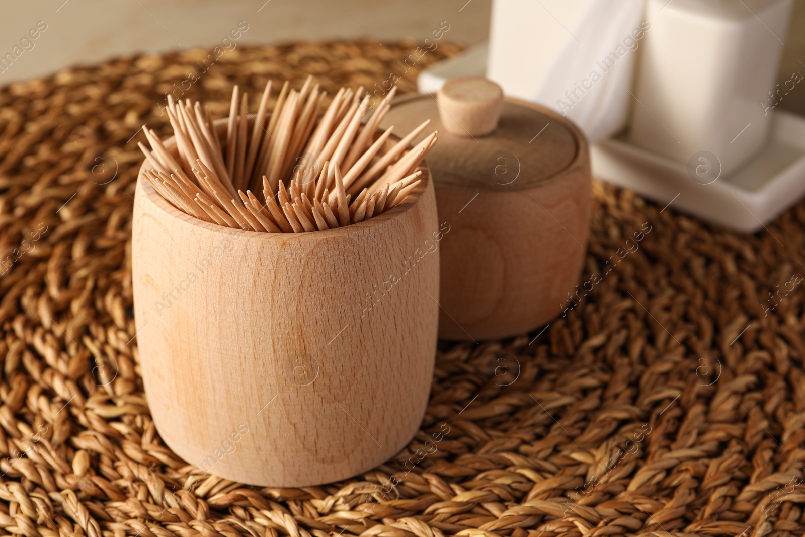 Photo of Wooden holder with many toothpicks on wicker mat, closeup