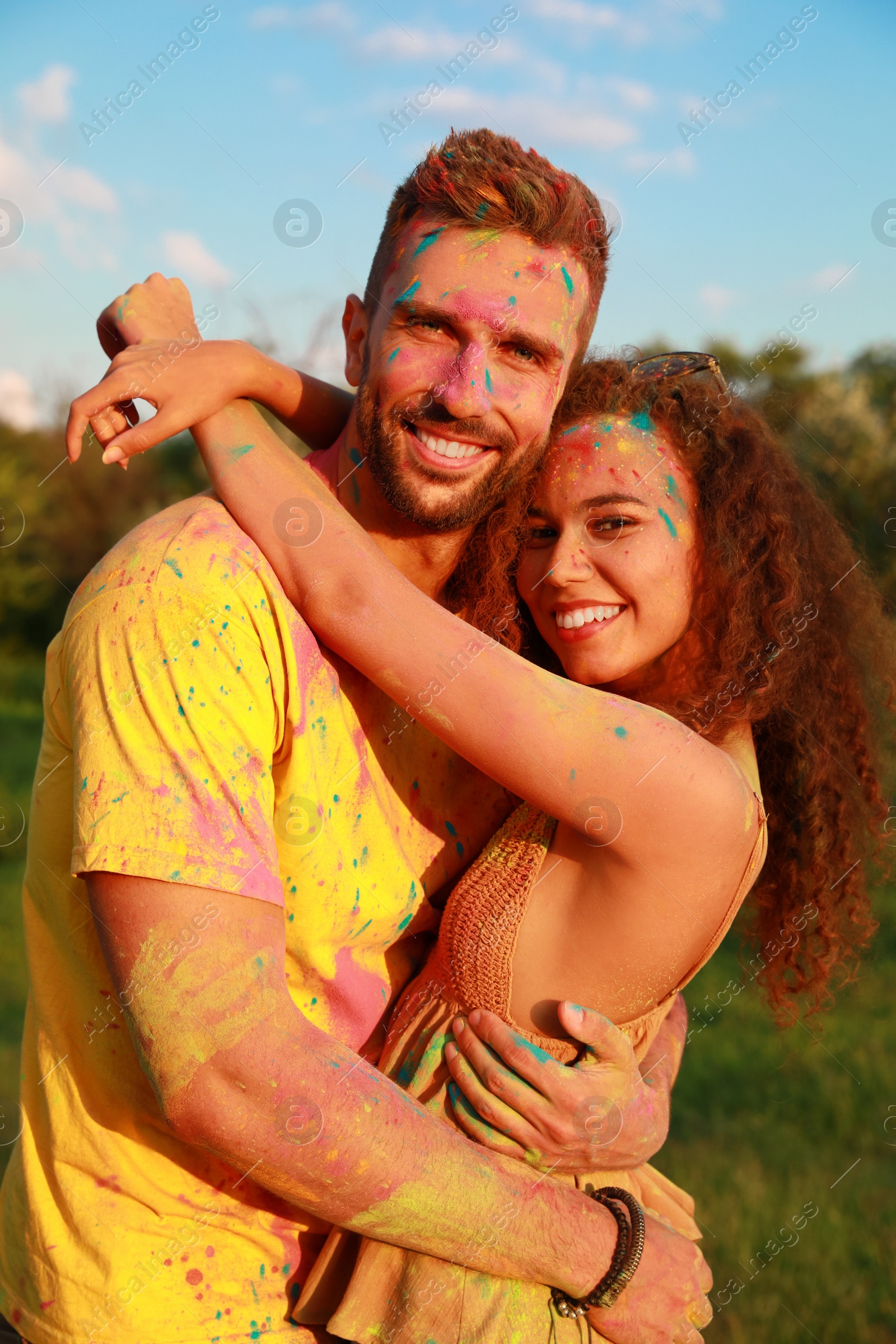 Photo of Happy couple covered with colorful powder dyes outdoors. Holi festival celebration