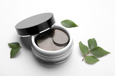 Photo of Under eye patches in jar near green leaves on white background. Cosmetic product