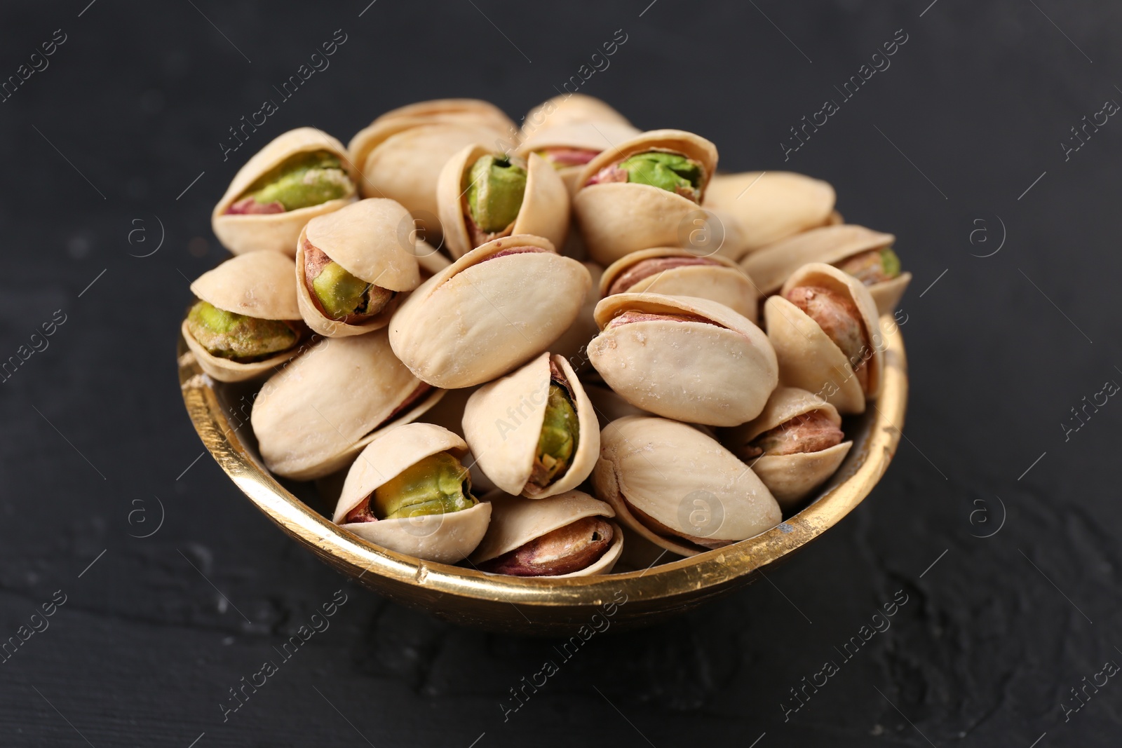 Photo of Tasty pistachios in bowl on black table, closeup