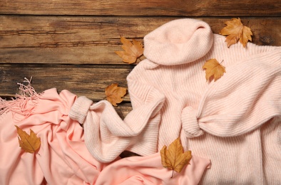 Photo of Pink sweater, scarf and dry leaves on wooden background, flat lay. Autumn season