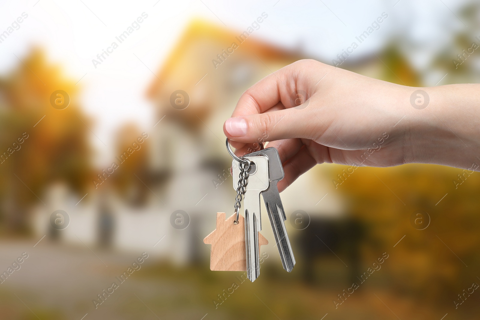 Image of Woman holding keys near house outdoors, closeup