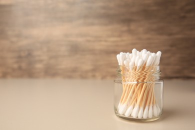Photo of Jar of clean cotton buds on beige background. Space for text