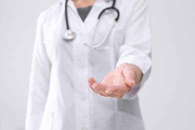 Young female doctor offering helping hand on white background