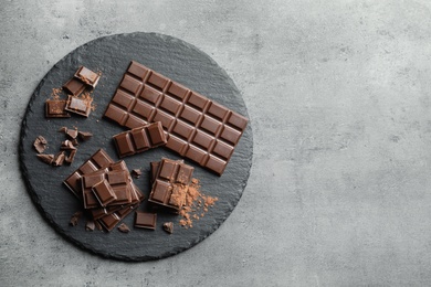 Photo of Slate plate with pieces of tasty chocolate on grey background, top view. Space for text