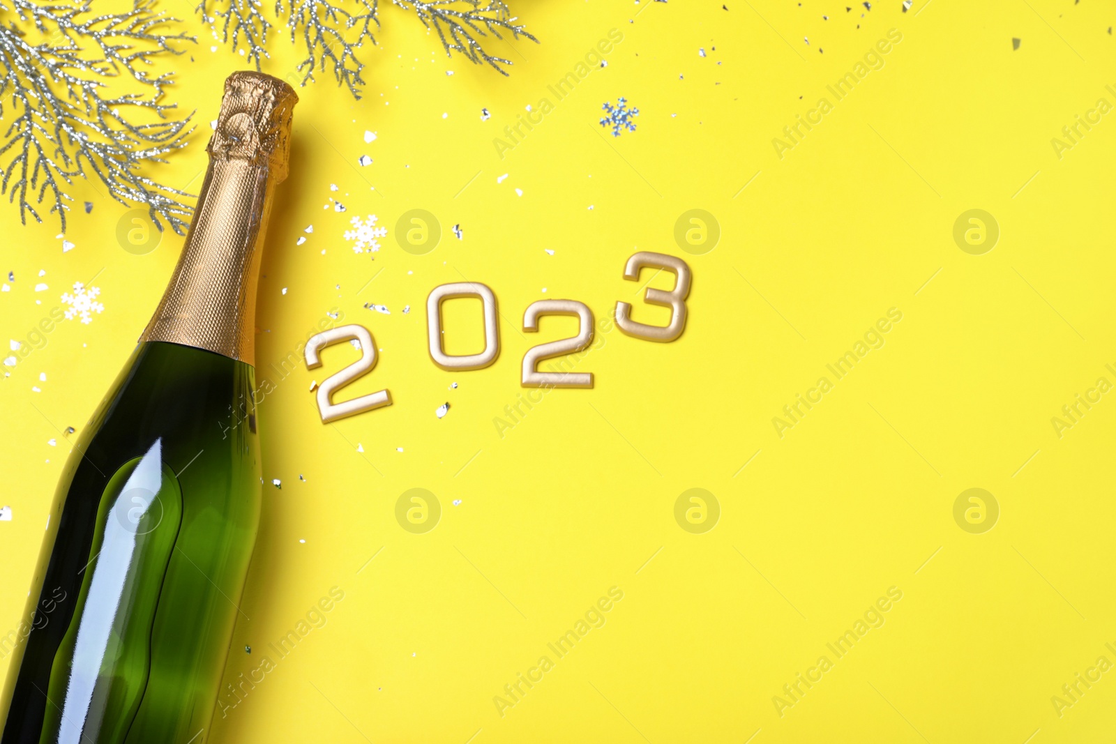 Photo of Happy New Year 2023! Flat lay composition with bottle of sparkling wine on yellow background, space for text