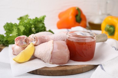 Fresh marinade, raw chicken drumsticks and lemon wedge on table, closeup
