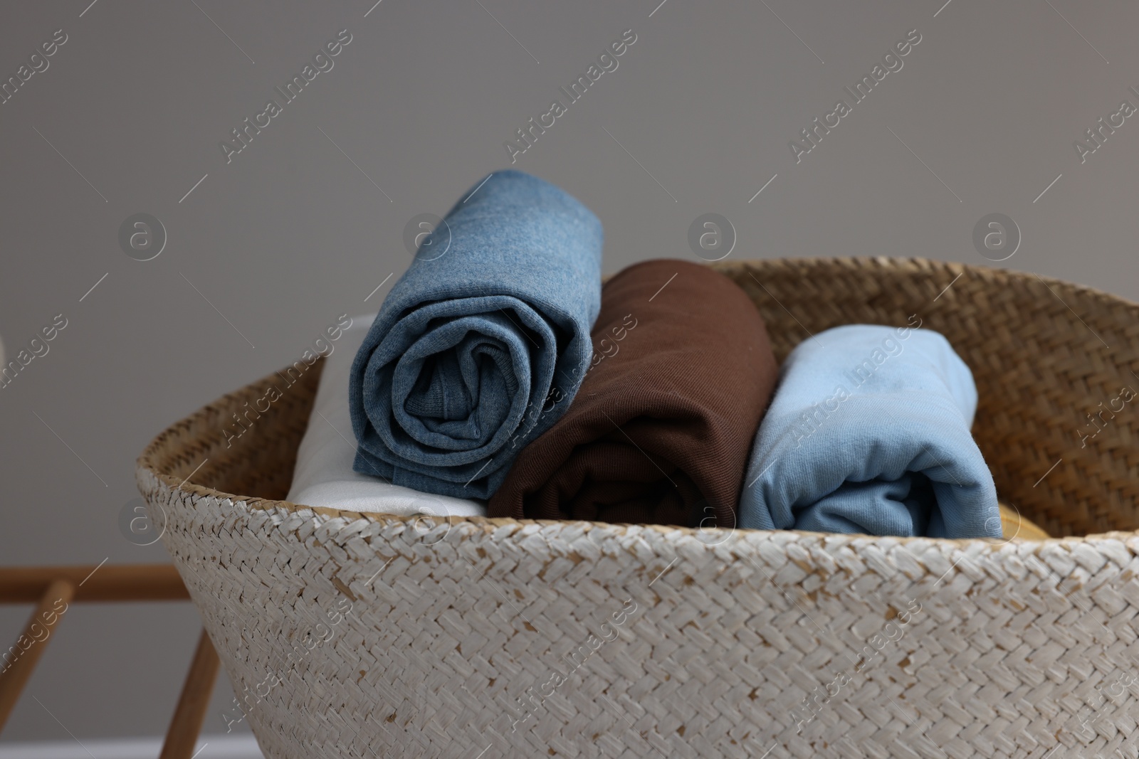 Photo of Different rolled shirts in basket against grey wall, closeup. Organizing clothes