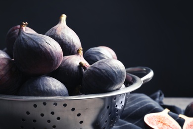 Colander with fresh ripe figs on table against black background, closeup