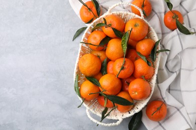 Photo of Basket with fresh ripe tangerines and leaves on grey table, flat lay. Space for text