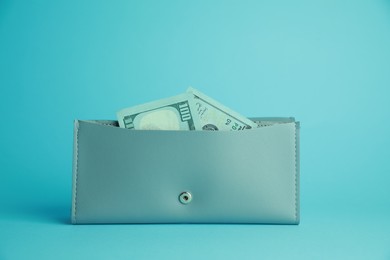 Stylish leather purse with dollar banknotes on light blue background