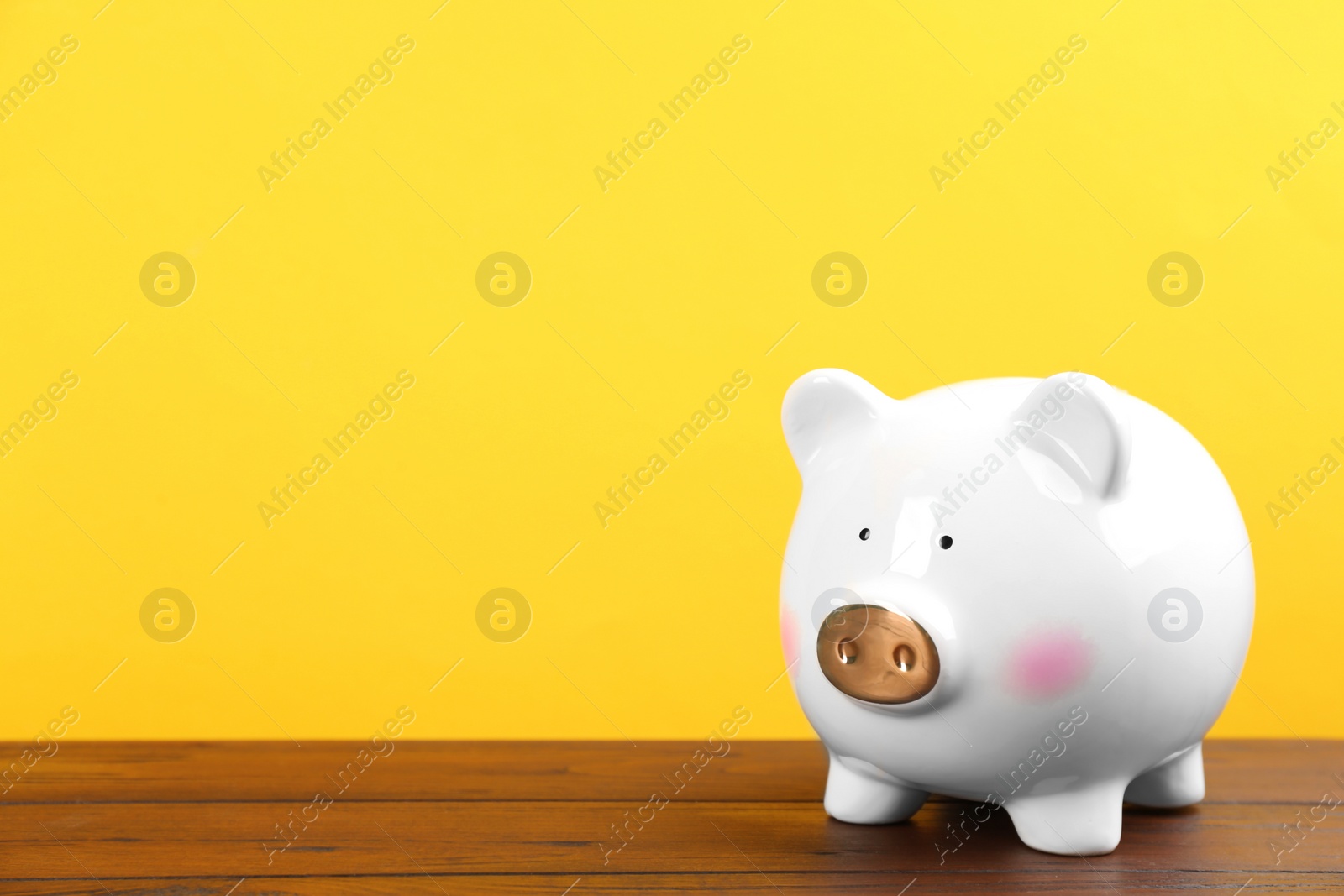 Photo of White piggy bank on wooden table against yellow background. Space for text