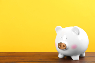 Photo of White piggy bank on wooden table against yellow background. Space for text