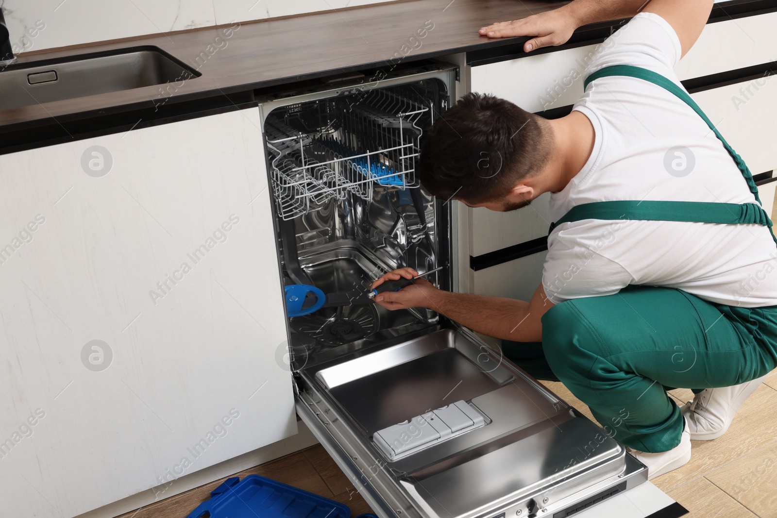 Photo of Serviceman repairing dishwasher with screwdriver in kitchen