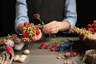 Photo of Florist making bouquet of dried flowers at wooden table, closeup