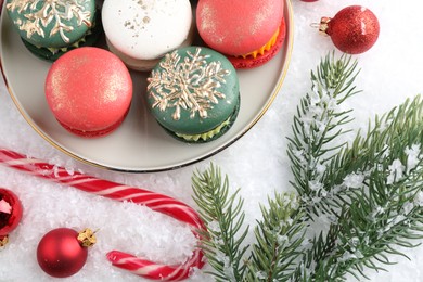 Photo of Beautifully decorated Christmas macarons, candy cane and festive decor on snow, flat lay