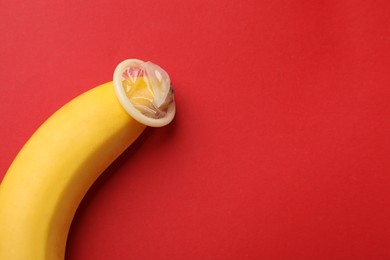 Photo of Banana with condom on red background, above view and space for text. Safe sex concept