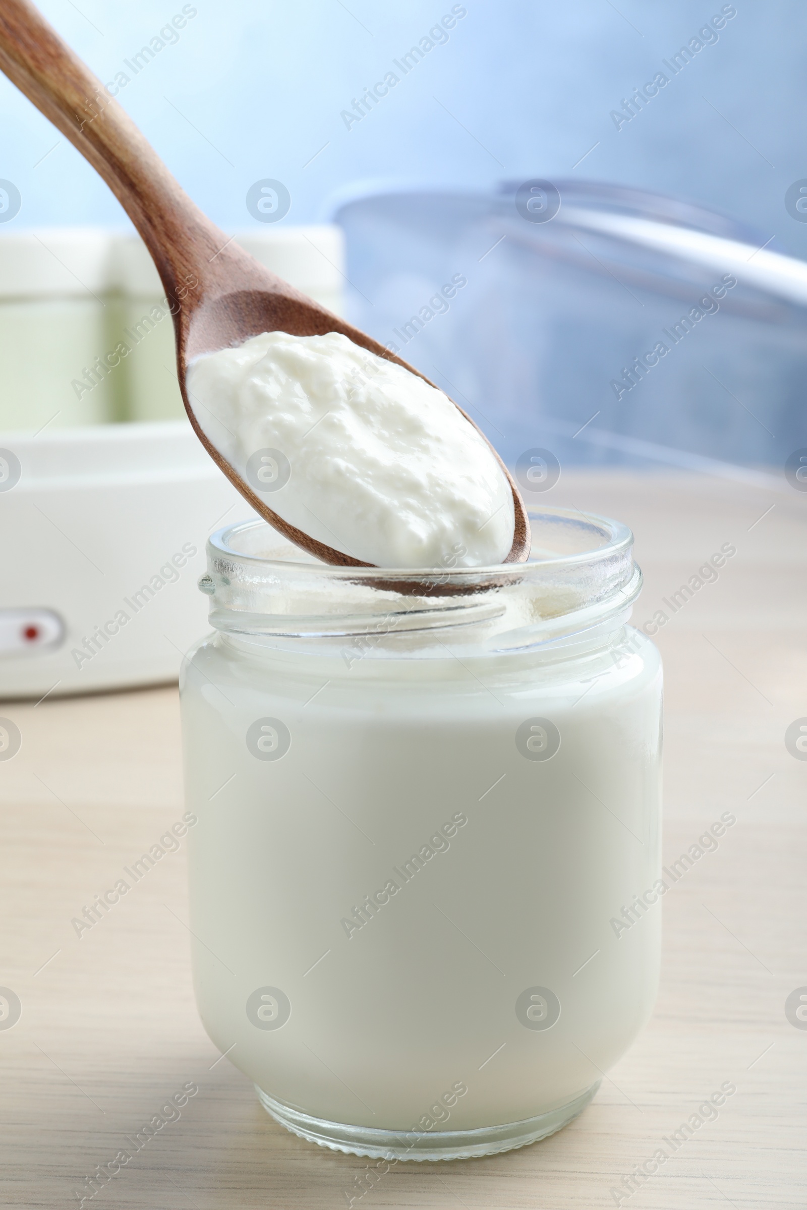 Photo of Spoon with tasty yogurt over glass jar on white wooden table