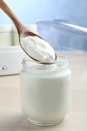 Spoon with tasty yogurt over glass jar on white wooden table