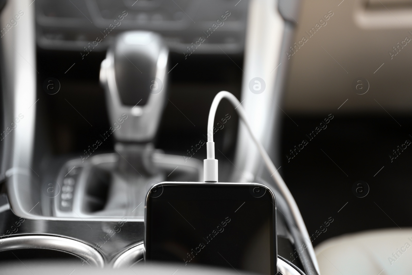 Photo of Mobile phone with charging cable in car, closeup