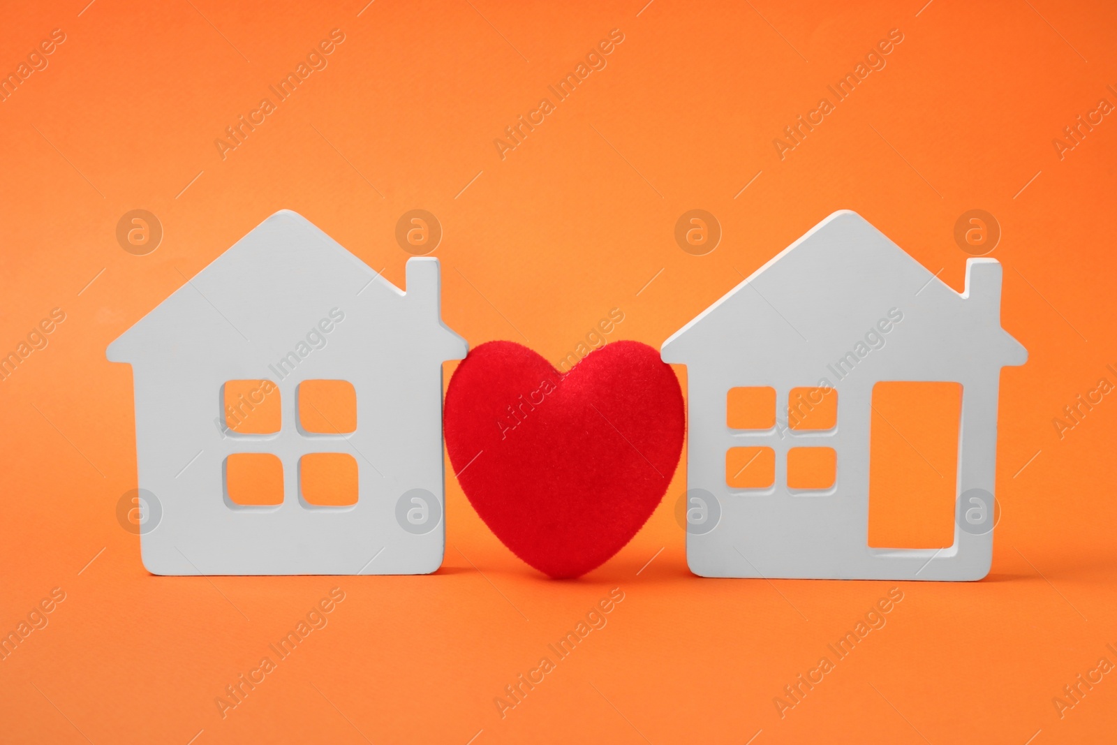 Photo of Long-distance relationship concept. Decorative heart between two white house models on orange background