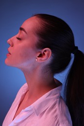 Portrait of beautiful young woman on blue background with neon lights