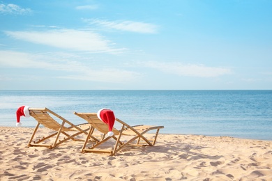 Photo of Sun loungers with Santa's hats on beach, space for text. Christmas vacation