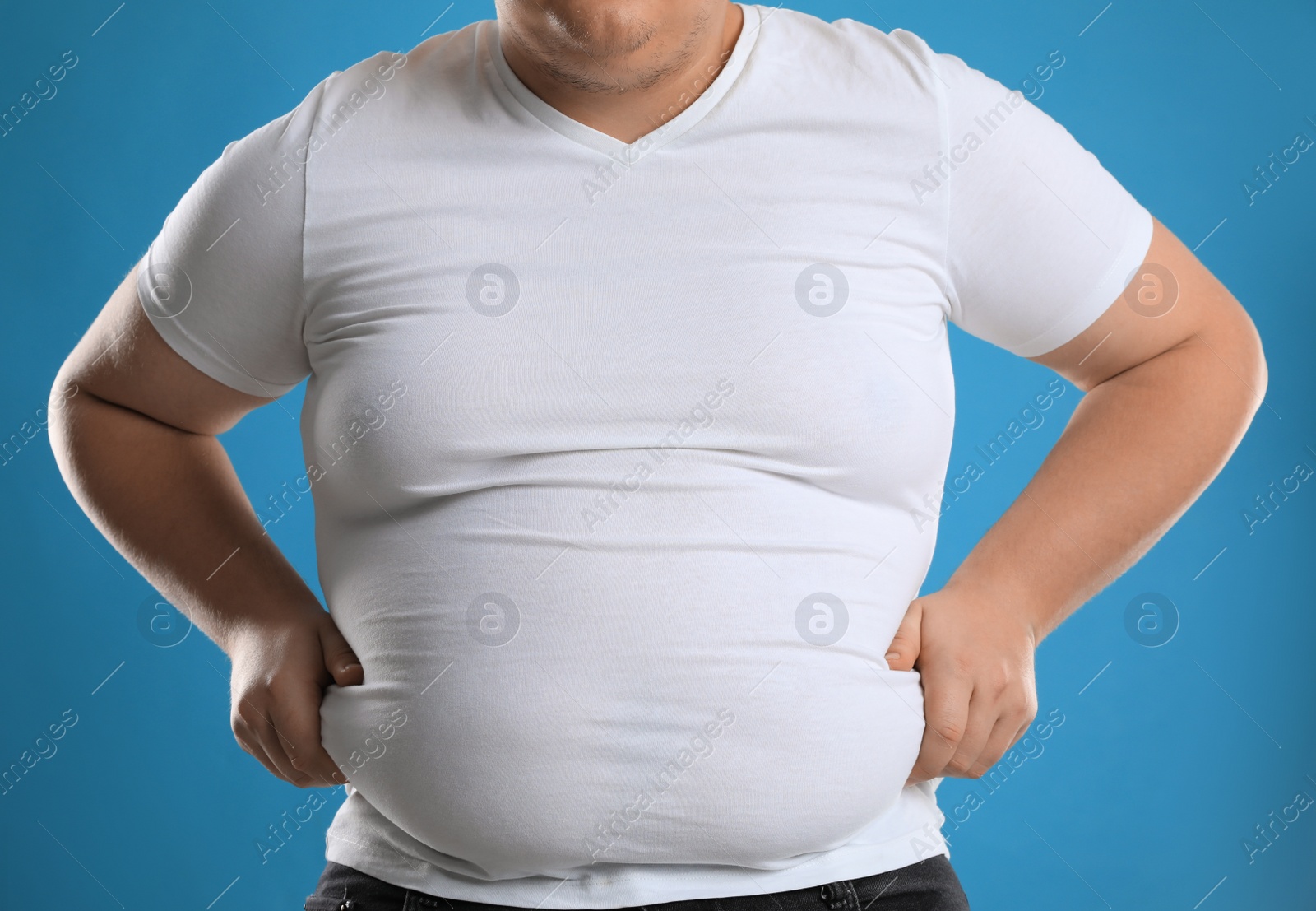 Photo of Overweight man in tight t-shirt on light blue background, closeup