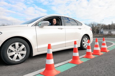 Photo of Young woman in car on test track with traffic cones. Driving school