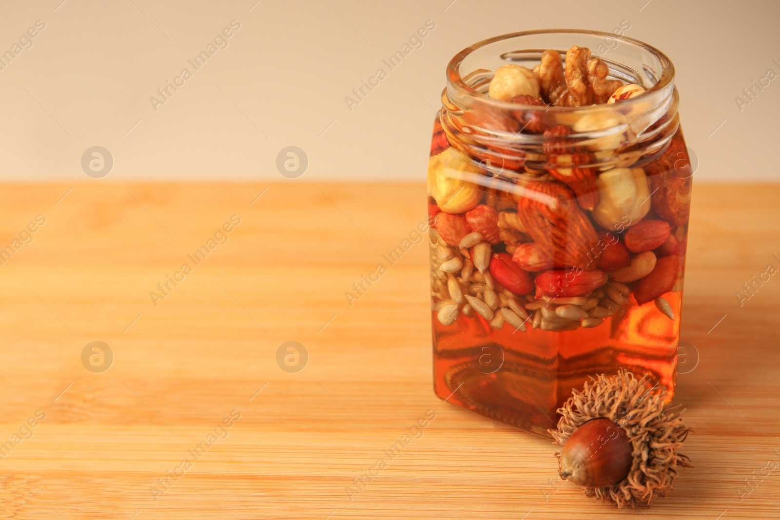 Photo of Different nuts with honey in jar and acorn on wooden table. Space for text