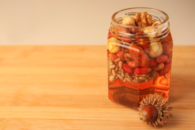 Different nuts with honey in jar and acorn on wooden table. Space for text