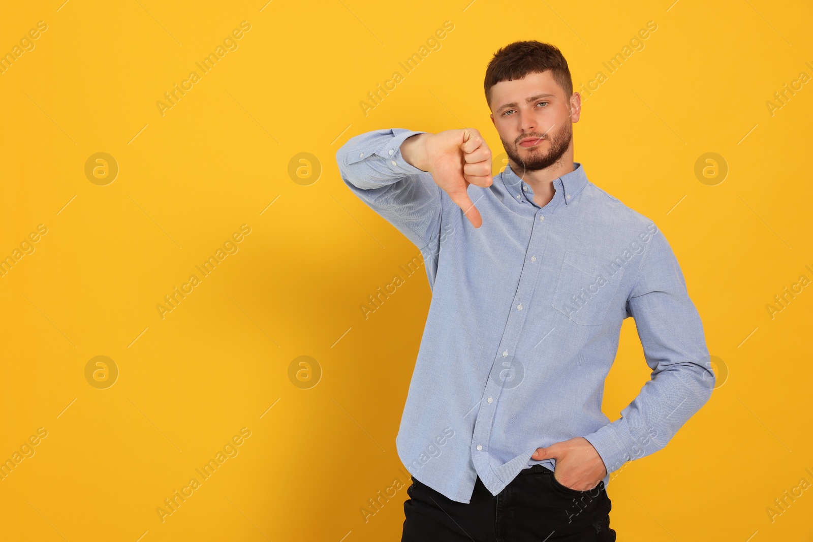 Photo of Young man showing thumb down on orange background, space for text