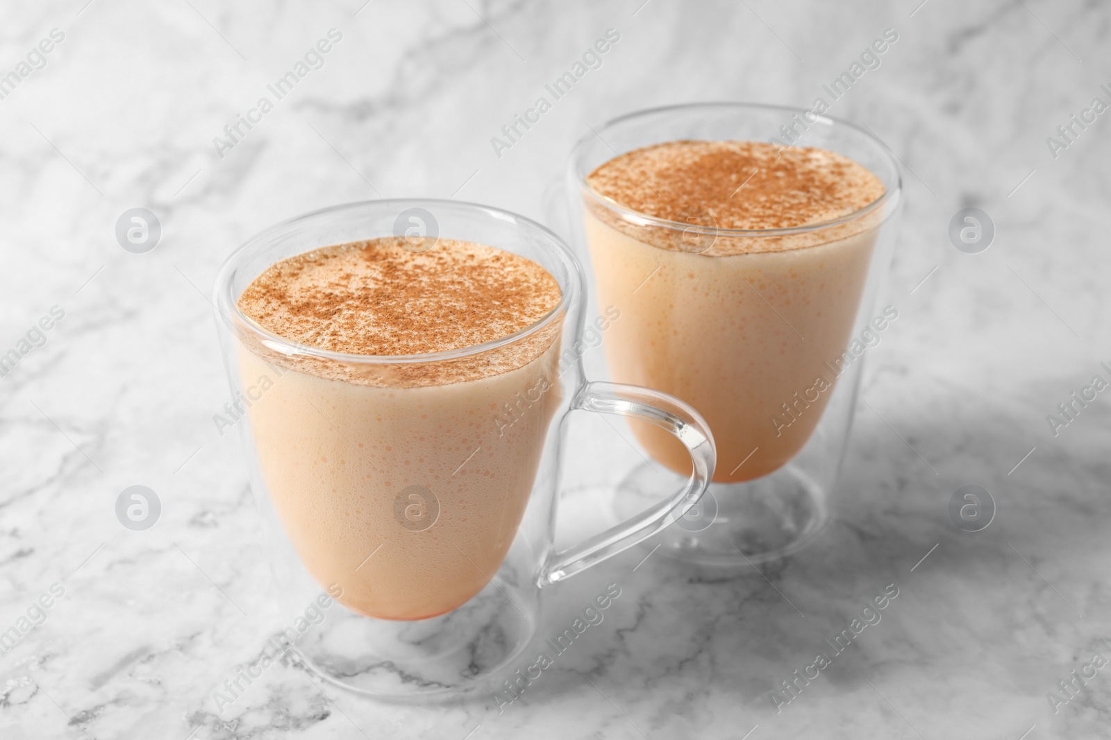 Photo of Glass cups of delicious eggnog on white marble table