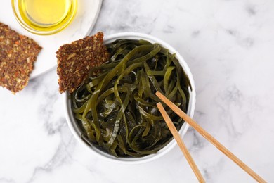 Photo of Tasty seaweed salad in bowl served on white marble table, flat lay