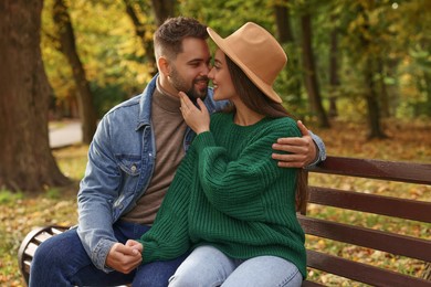 Happy young couple spending time together on wooden bench in autumn park