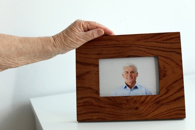 Photo of Elderly woman with framed photo of her son indoors, closeup