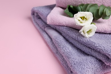 Photo of Soft folded towels with flowers and eucalyptus branch on pink background, closeup. Space for text