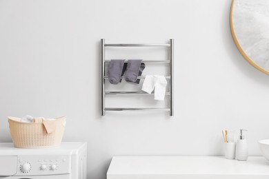 Photo of Heated towel rail with socks on white wall in bathroom