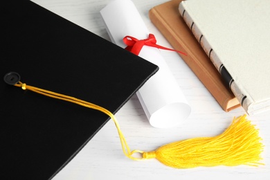 Graduation hat and student's diploma on white wooden table, above view