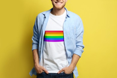 Young man wearing white t-shirt with image of LGBT pride flag on yellow background