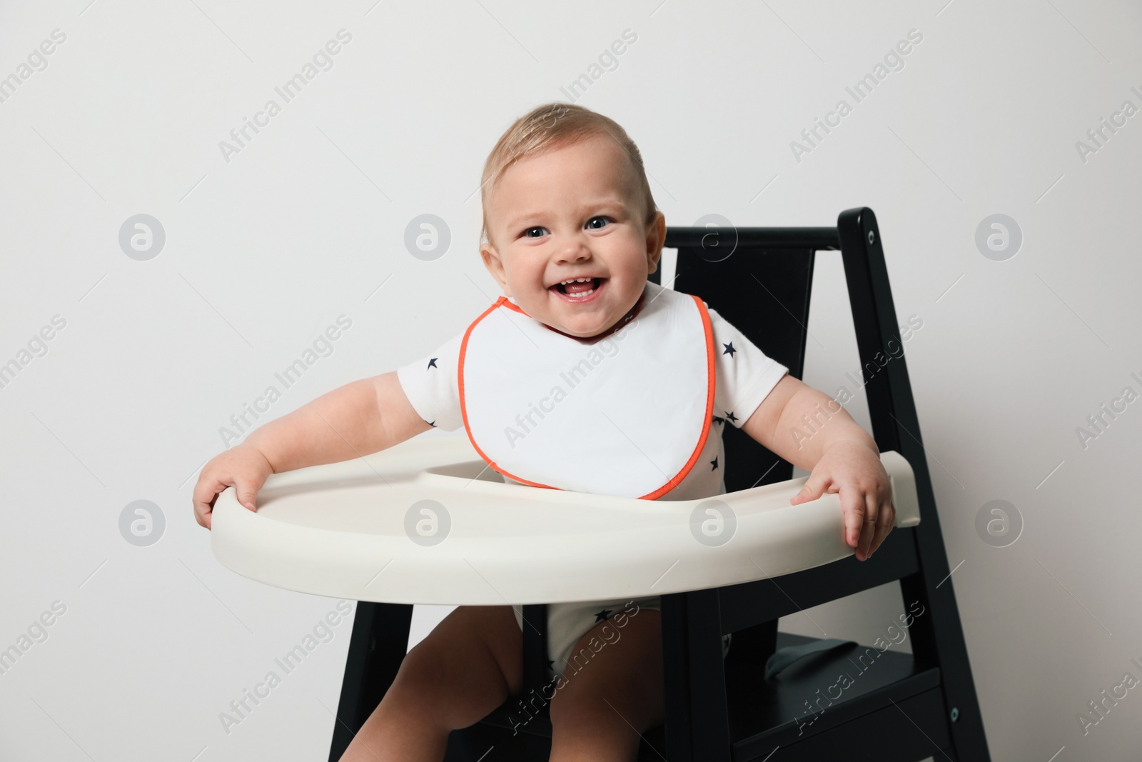 Photo of Cute little baby wearing bib in highchair on white background