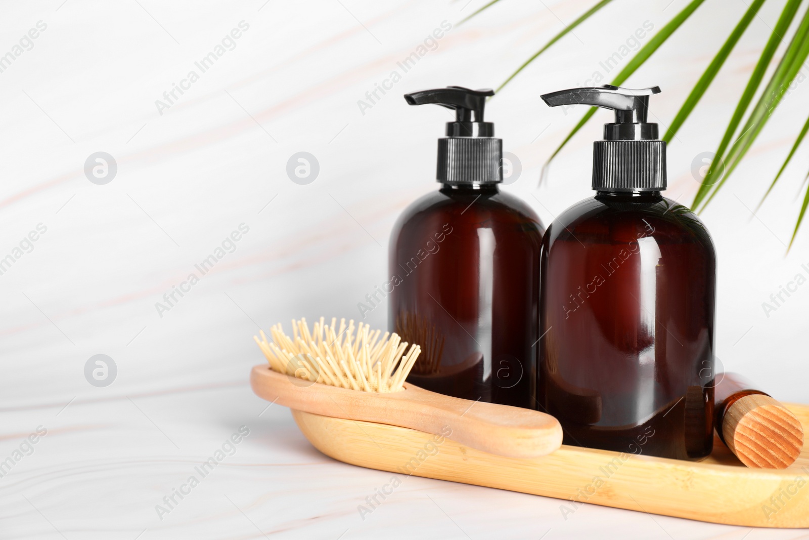 Photo of Shampoo bottles, wooden brush and essential oil on white marble table, space for text