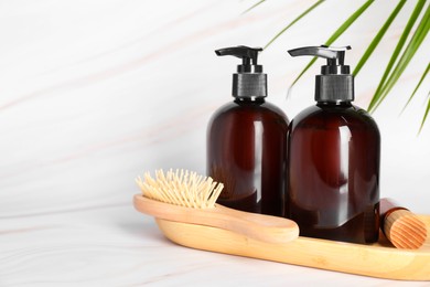 Shampoo bottles, wooden brush and essential oil on white marble table, space for text