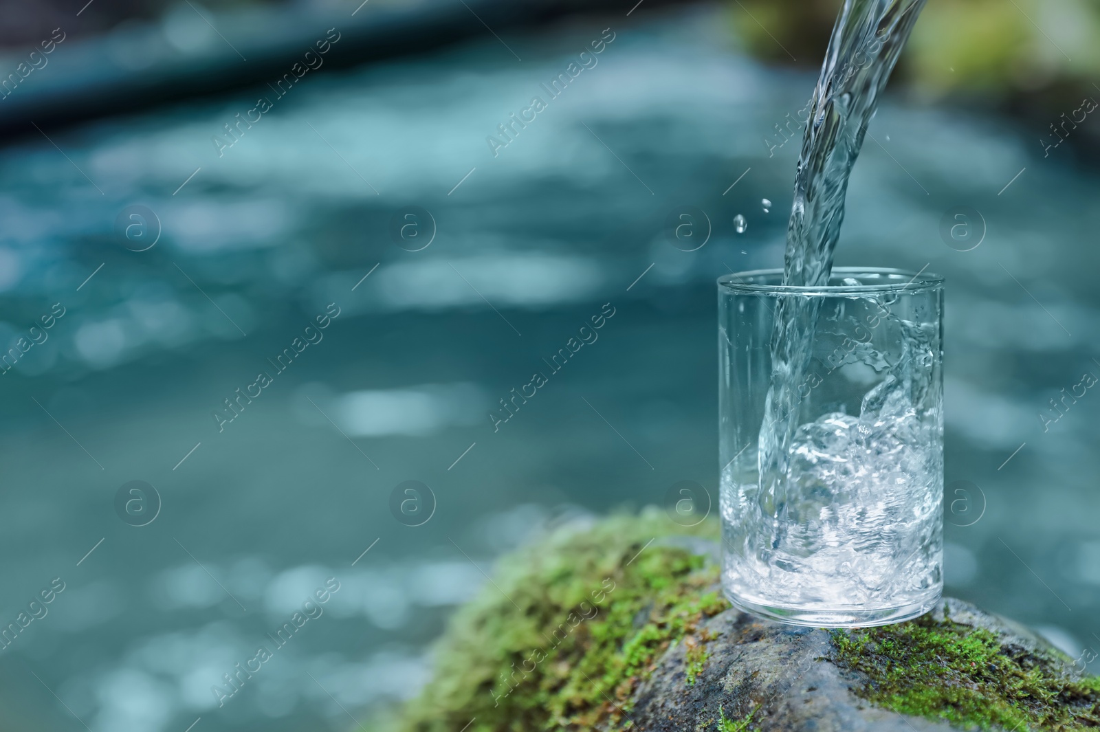 Photo of Fresh water pouring into glass on stone near river. Space for text