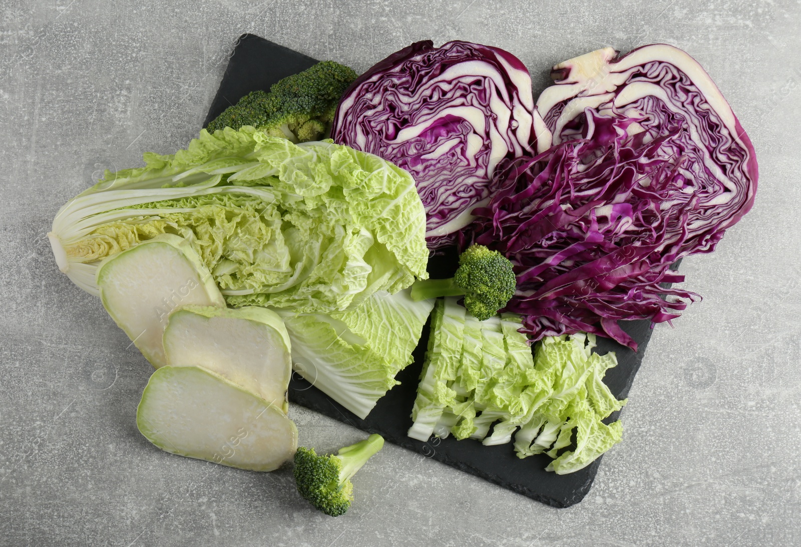 Photo of Different types of cut cabbage on light grey table, flat lay