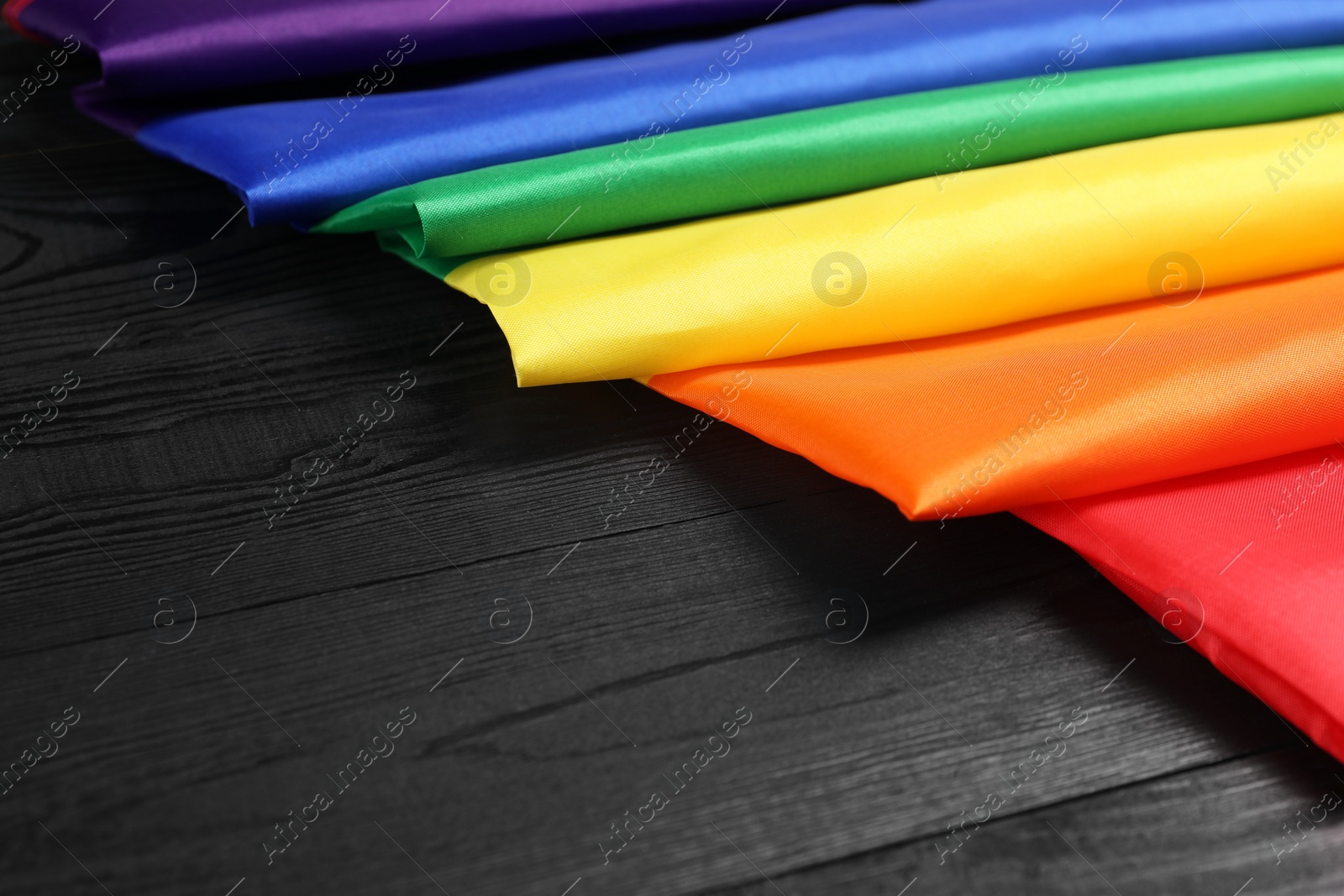 Photo of Rainbow LGBT flag on black wooden background, closeup. Space for text